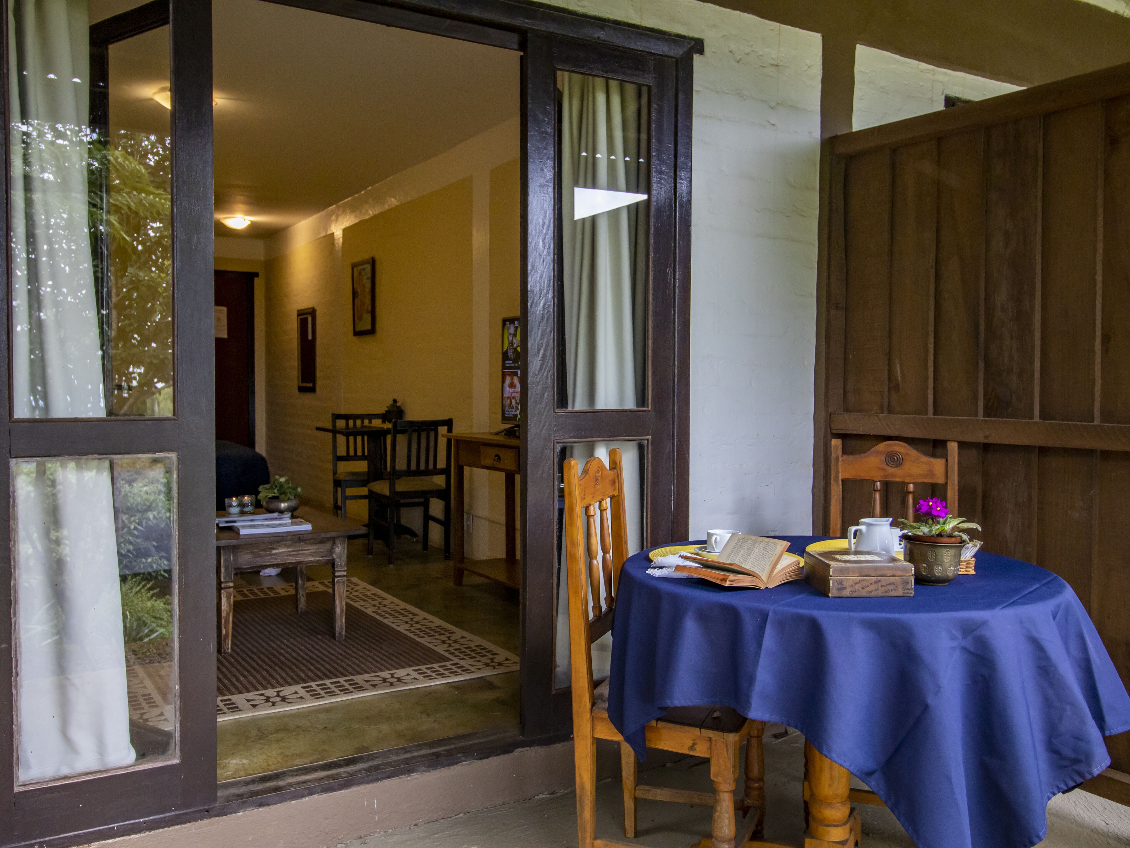 Une pièce avec une table recouverte d’une nappe bleue, des chaises en bois et une porte en bois donnant sur une autre pièce.