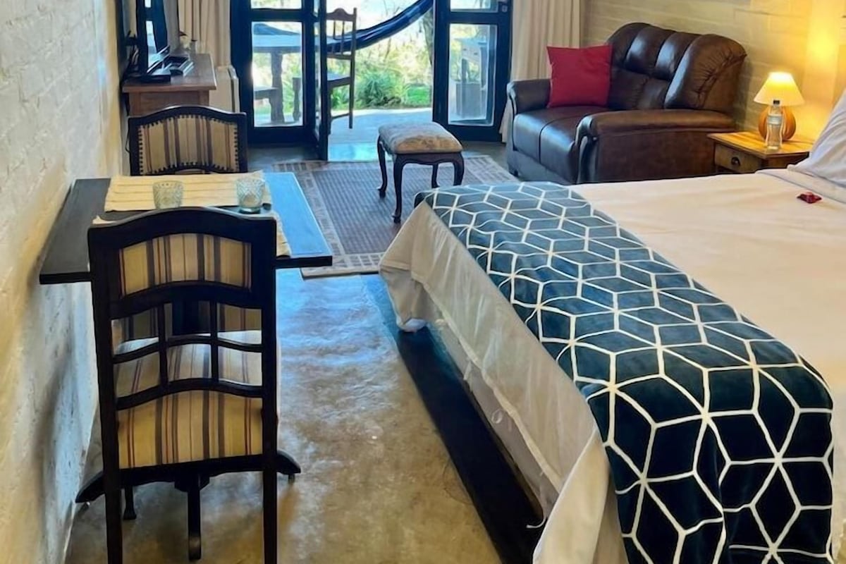 A hotel room with a bed, a desk, a chair, a sofa, and a view through a glass door.