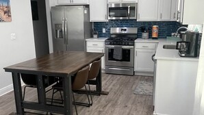 A modern kitchen with white cabinets, a stainless steel refrigerator, a microwave, and a gas stove.