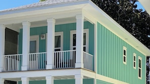 A two-story building with a balcony on the second floor, a front porch, and a small garden area.