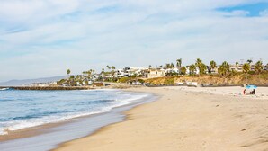Una playa con una hilera de casas, algunas con palmeras, y un rompeolas rocoso.