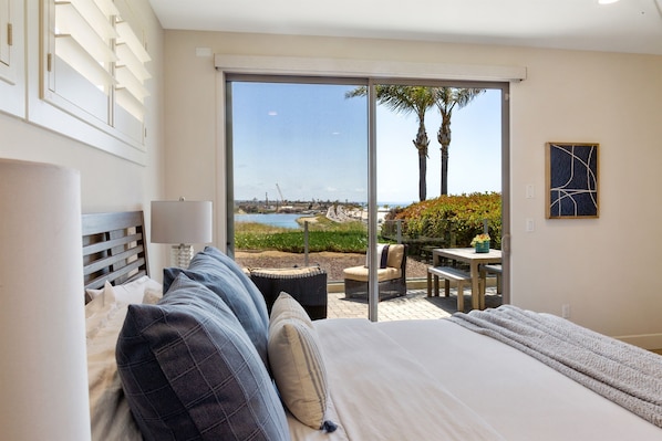 A bedroom with a large bed, a view of the beach, and a patio area with outdoor furniture.