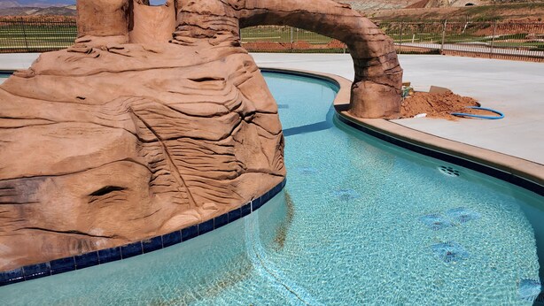 Une piscine au design naturel, agrémentée de rochers, entourée d’une zone délimitée par une clôture et offrant en arrière-plan un paysage montagneux.