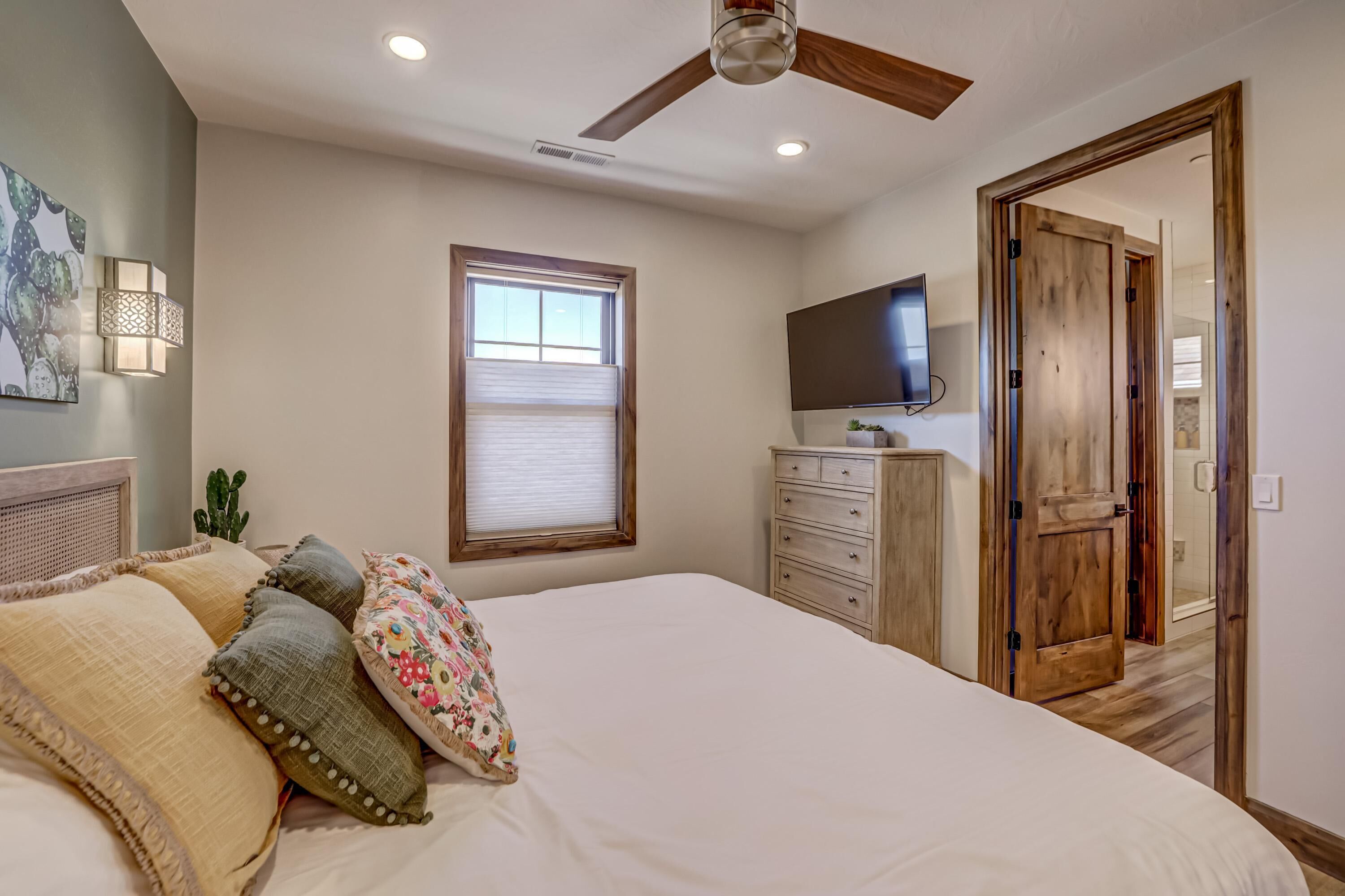 Un dormitorio con cama, ventilador de techo, ventana, cómoda y televisor.