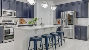A modern kitchen with dark blue cabinets, stainless steel appliances, a central island with stools, and pendant lighting. - 5 Suites | Mini Golf | Heated Pool | Lazy River | SKY (Washington)