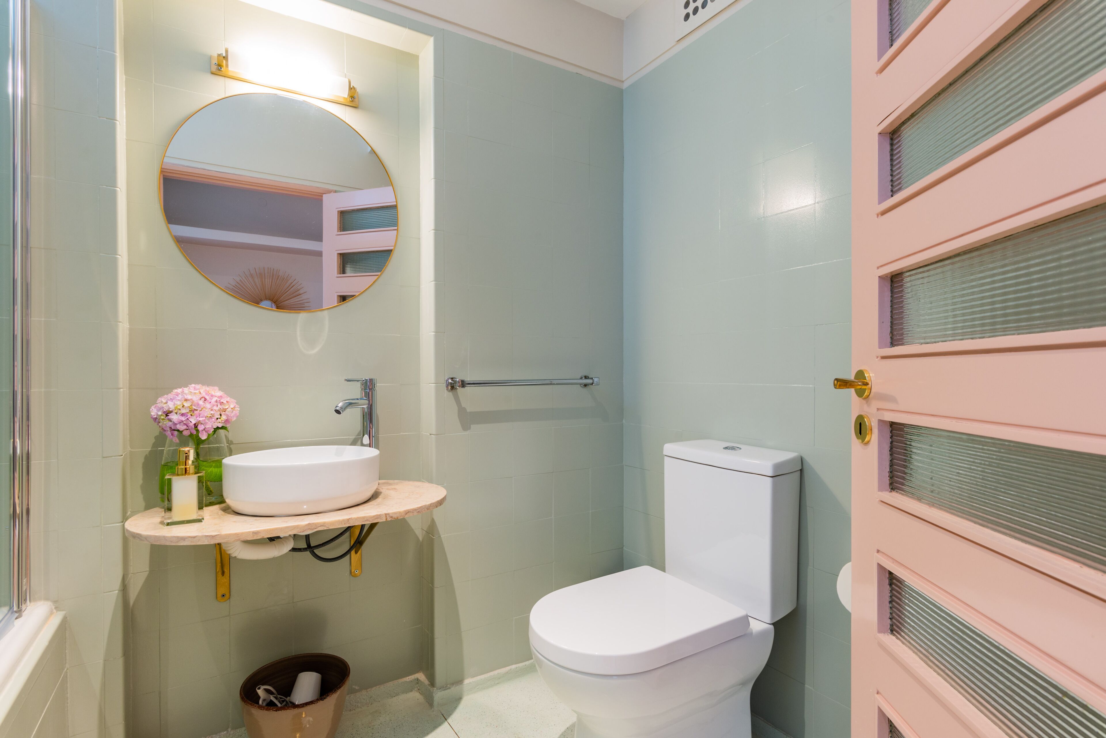 Une salle de bain avec un miroir rond, un lavabo, des toilettes et une porte rose.