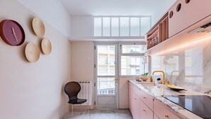 Une cuisine moderne avec des armoires roses, une chaise noire et un comptoir blanc.