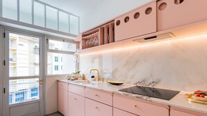 Une cuisine moderne avec des meubles roses, un plan de travail en marbre et une fenêtre donnant sur un balcon.