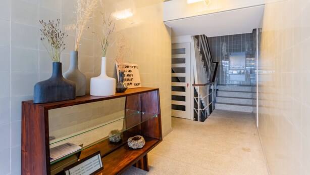 Un espace d’accueil avec une console en bois où sont exposés des vases et une pancarte de bienvenue, une vitrine et un escalier menant à un niveau supérieur.