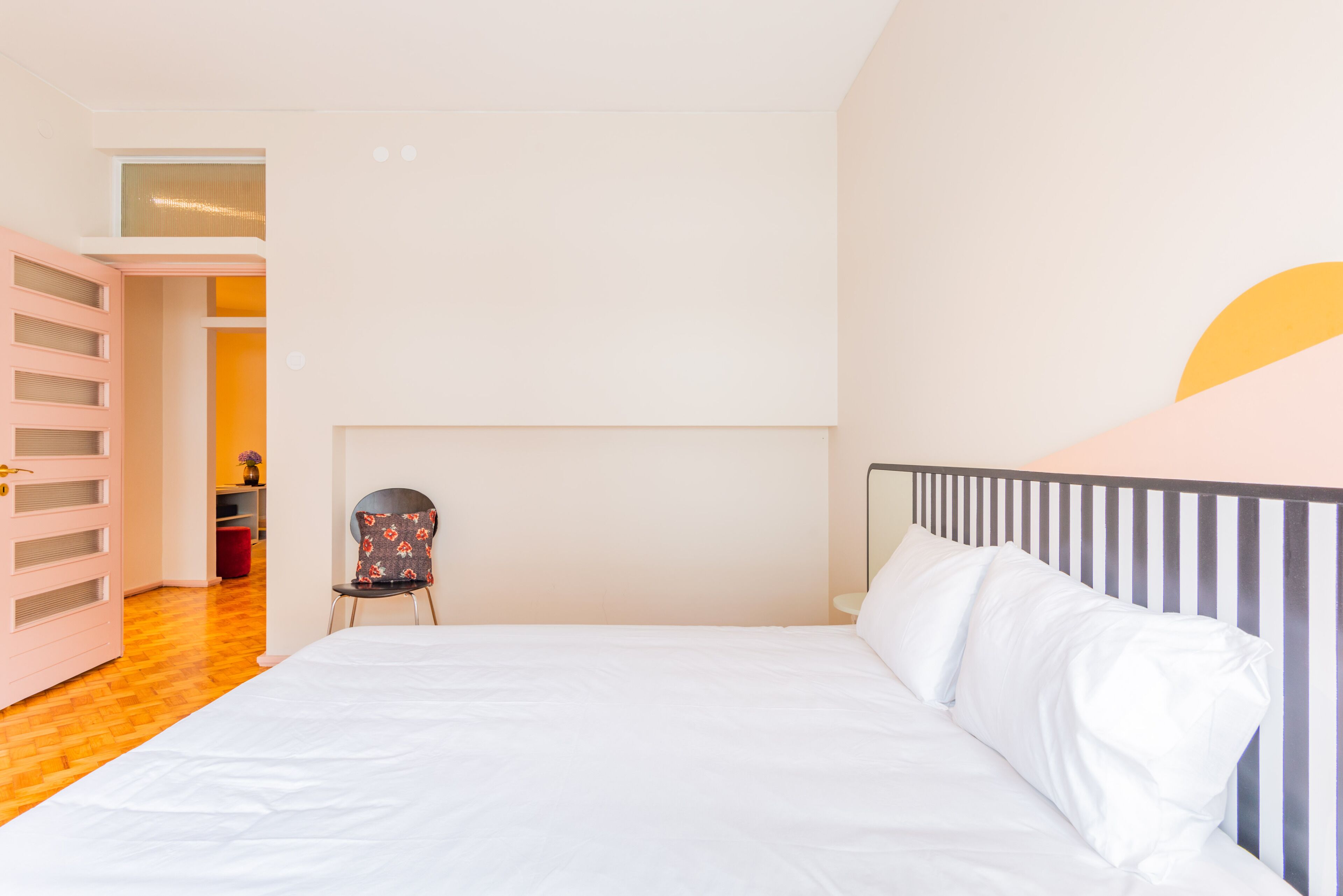 A bedroom with a bed, a chair, and a pink wardrobe.