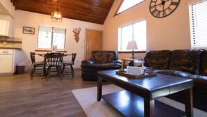 A cozy living room with a wooden ceiling, a leather sofa, a dining table with chairs, and a wall clock. - Moon Creek, A lovely Cabin that is located in the Pinetop Country Club Community (Pinetop)
