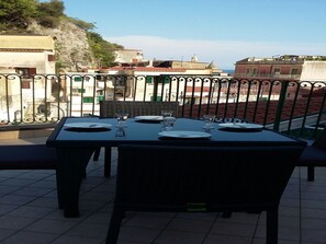 Une table à manger installée à l’extérieur, avec des chaises, donnant sur des bâtiments et agrémentée d’une rambarde.