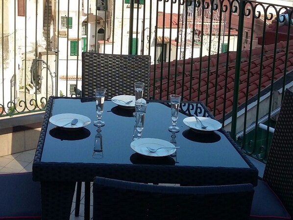 A table set for four with chairs, a balcony railing, and buildings in the background.