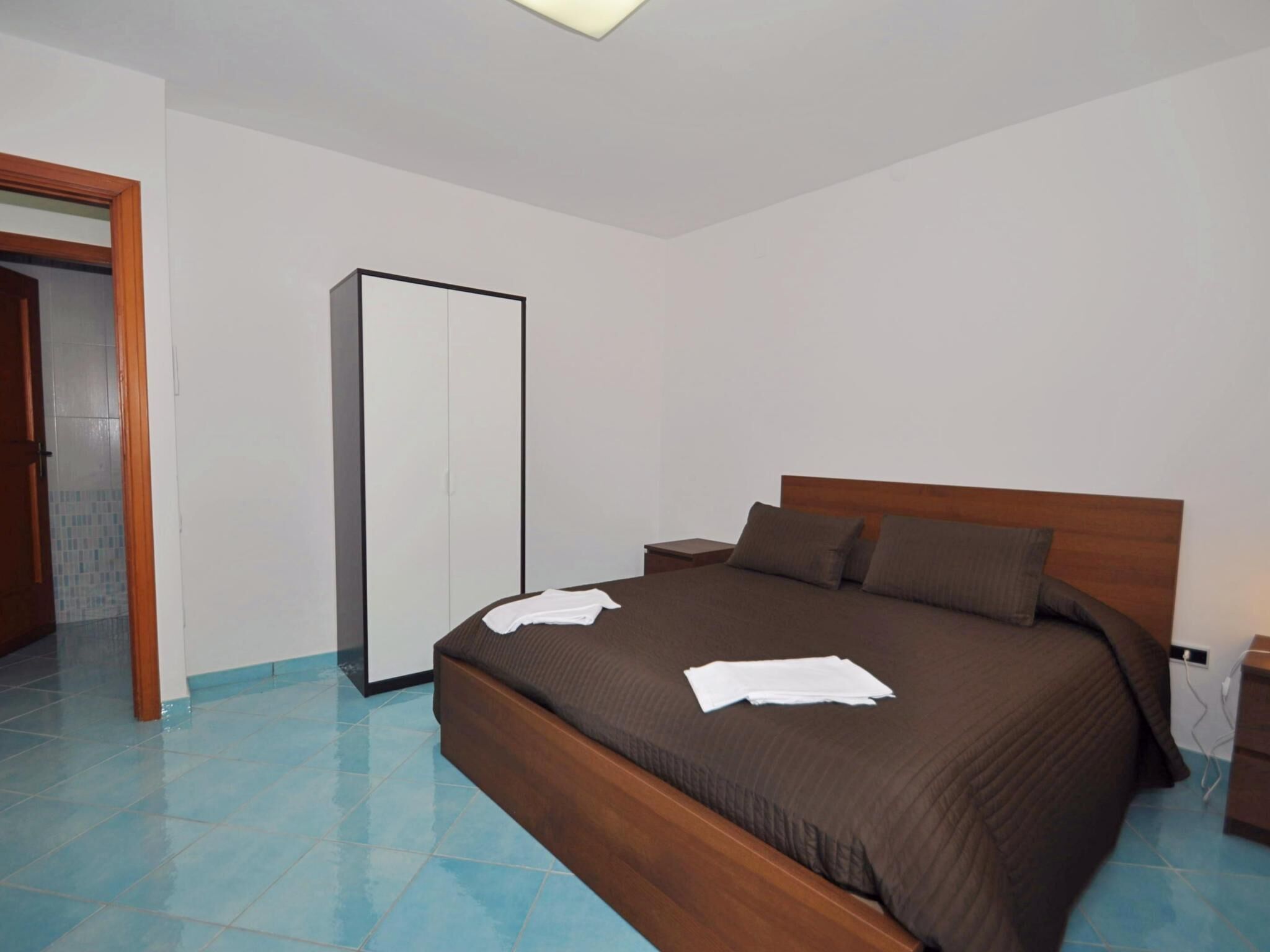 Un dormitorio con cama de madera, armario y suelo de baldosas.