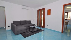 A modern living room with a grey sectional sofa, a glass coffee table, and a blue tiled floor. - Apartment in the heart of Cetara (Cetara)