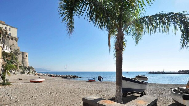 A beach with boats, a palm tree, and a historic building. - B&B in the heart of Cetara - Standard Double room (Cetara)