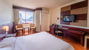 A hotel room with a bed, a desk, two chairs, a television, and a window with curtains.