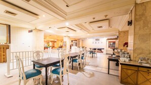 A spacious dining area with multiple tables and chairs, a kitchen counter with dishes, and a decorative wall.