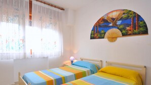 Una habitación con dos camas, una ventana con cortinas translúcidas y un cuadro colgado en la pared de un paisaje.