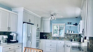 Una cocina con armarios blancos, una silla de madera y una ventana con persianas.