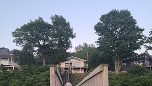 Un puente de madera que lleva a una casa con balcón, rodeada de árboles y vegetación.