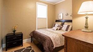 A bedroom with a bed, bedside table, lamp, and a window with blinds. - Roscoe Village- Only steps to cute shops & dining! Sleeps 4-6 (Chicago)