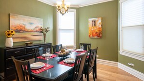 A dining room with a dark wooden table set for four, surrounded by black chairs. There is a chandelier above the table, and artwork is displayed on the walls. - Roscoe Village- Only steps to cute shops & dining! Sleeps 4-6 (Chicago)