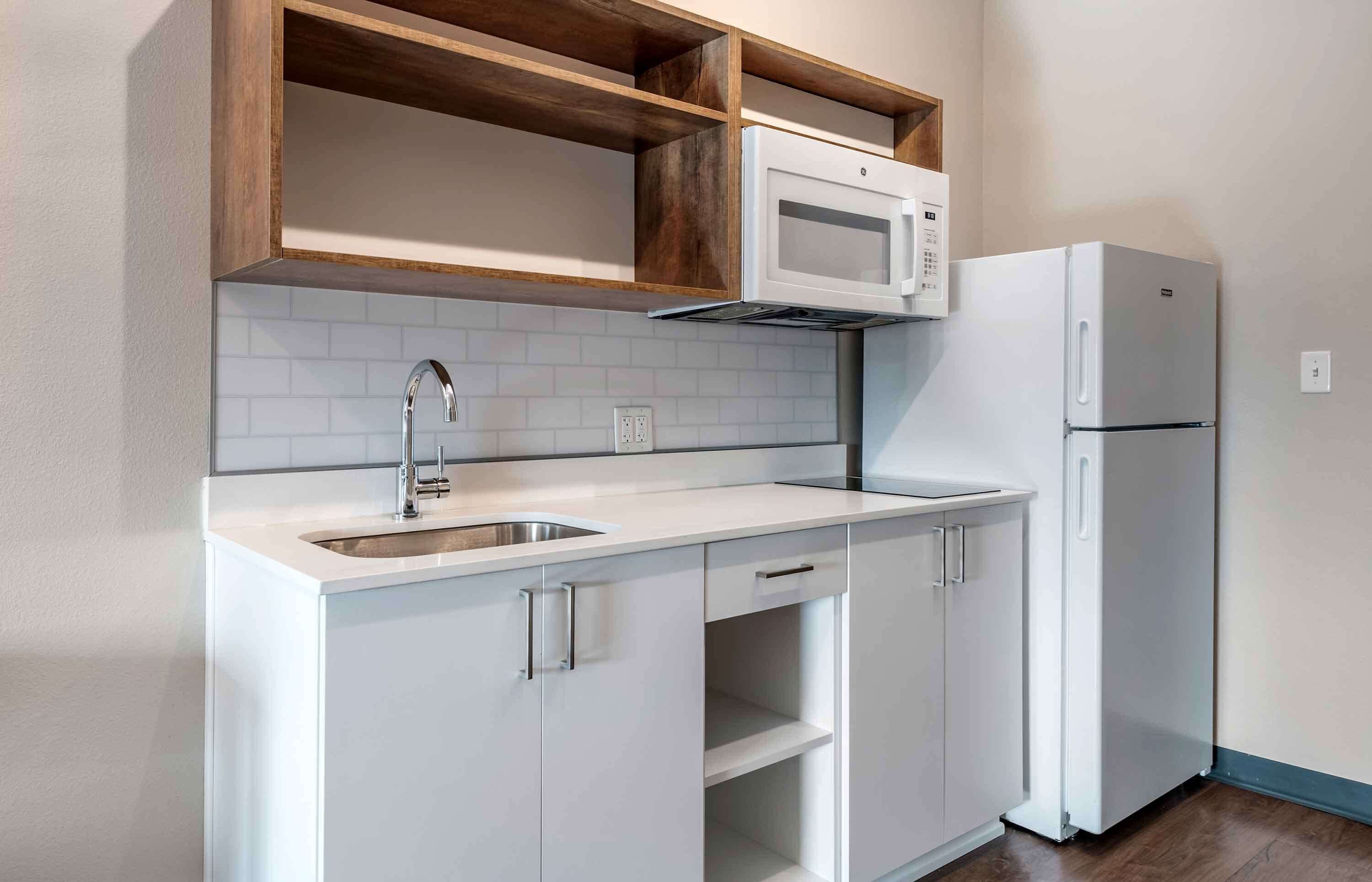 A compact kitchen with white cabinets, a stainless steel sink, a microwave, and a refrigerator.