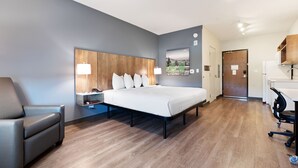 Una habitación de hotel moderna con una cama grande, un escritorio, una silla y una pequeña zona de estar.