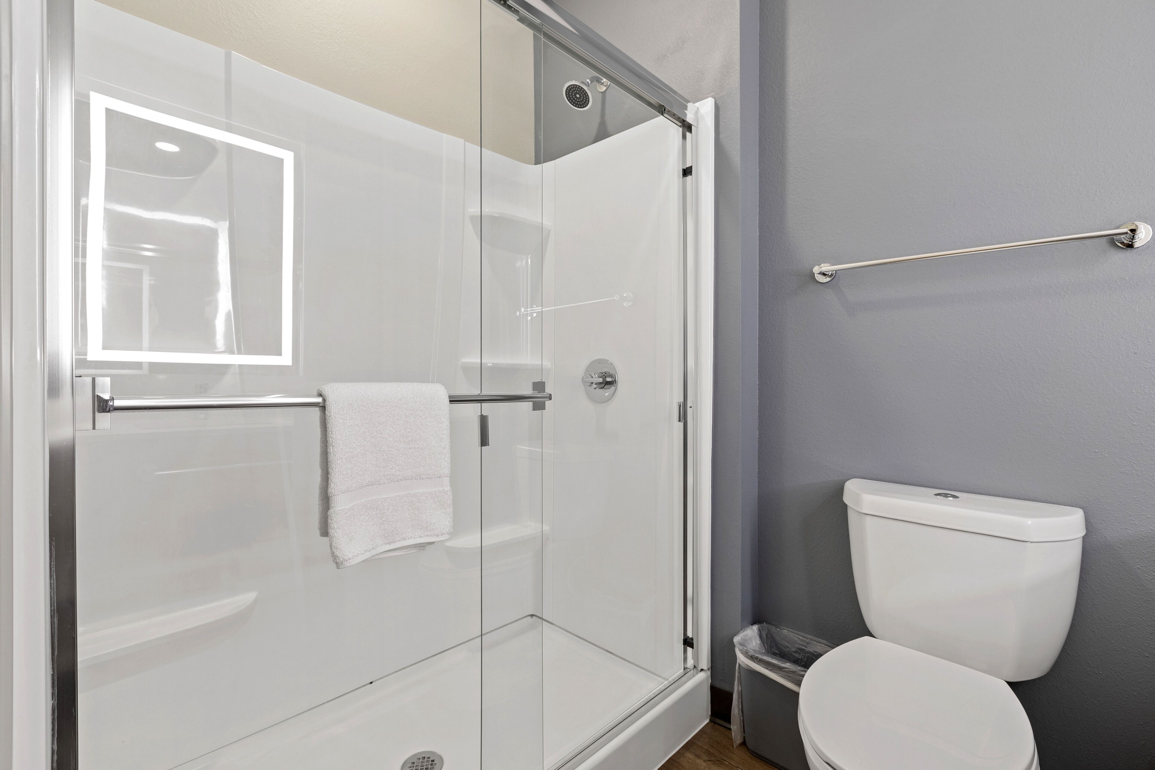 A modern bathroom with a glass-enclosed shower, a white toilet, and a handrail.