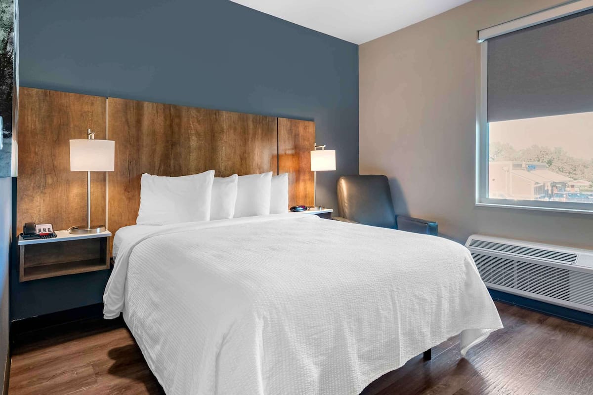Une chambre d’hôtel avec un grand lit, deux tables de chevet avec des lampes, une fenêtre donnant sur un beau paysage et un climatiseur fixé au mur.
