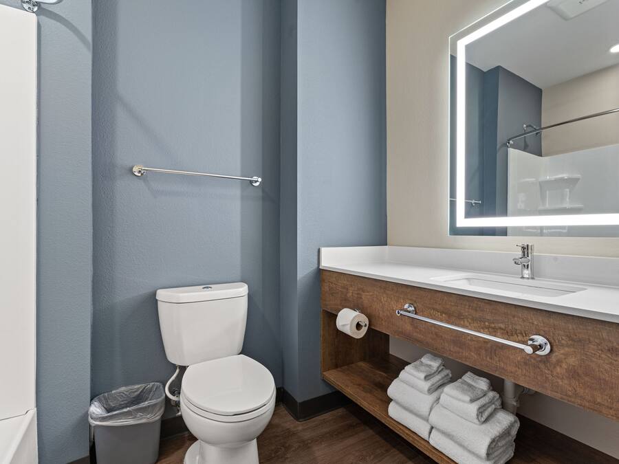 Un baño moderno con inodoro blanco, tocador de madera con espejo y toallero.