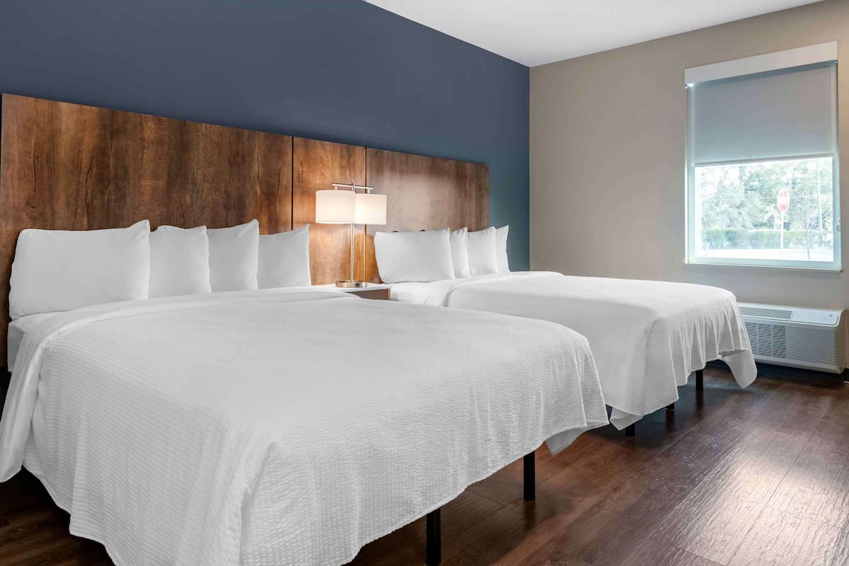 Une chambre d’hôtel avec deux lits, une tête de lit en bois, une lampe de chevet et une fenêtre donnant sur un paysage verdoyant.