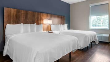 A hotel room with two beds, a wooden headboard, a bedside lamp, and a window with a view of greenery.