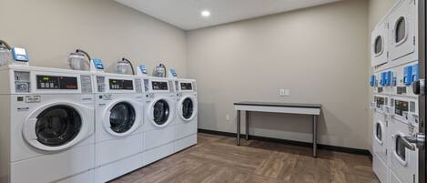 A laundry room with multiple washing machines and dryers, a table, and a wooden floor.