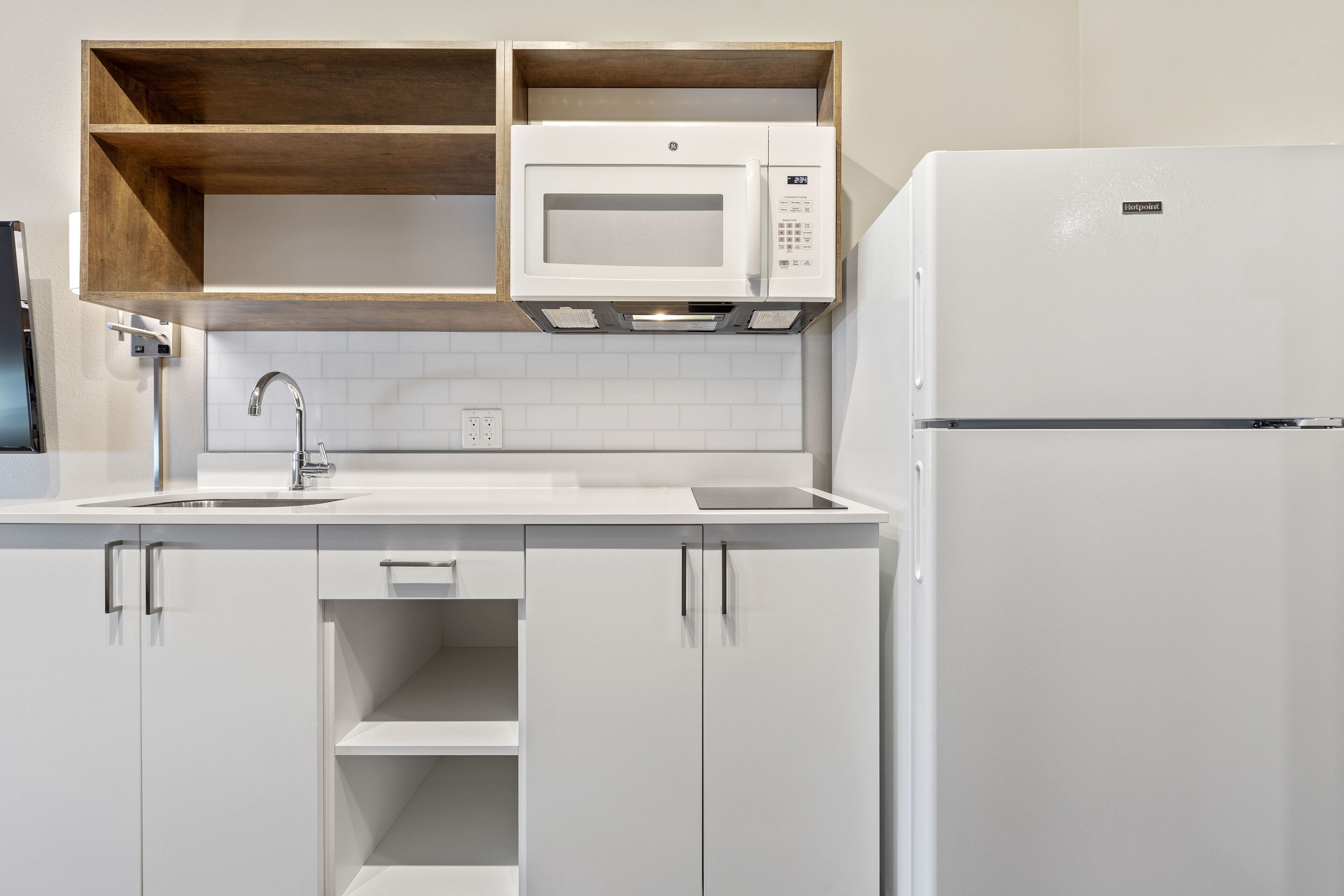 Una cocina moderna con armarios blancos, microondas integrado y refrigerador.