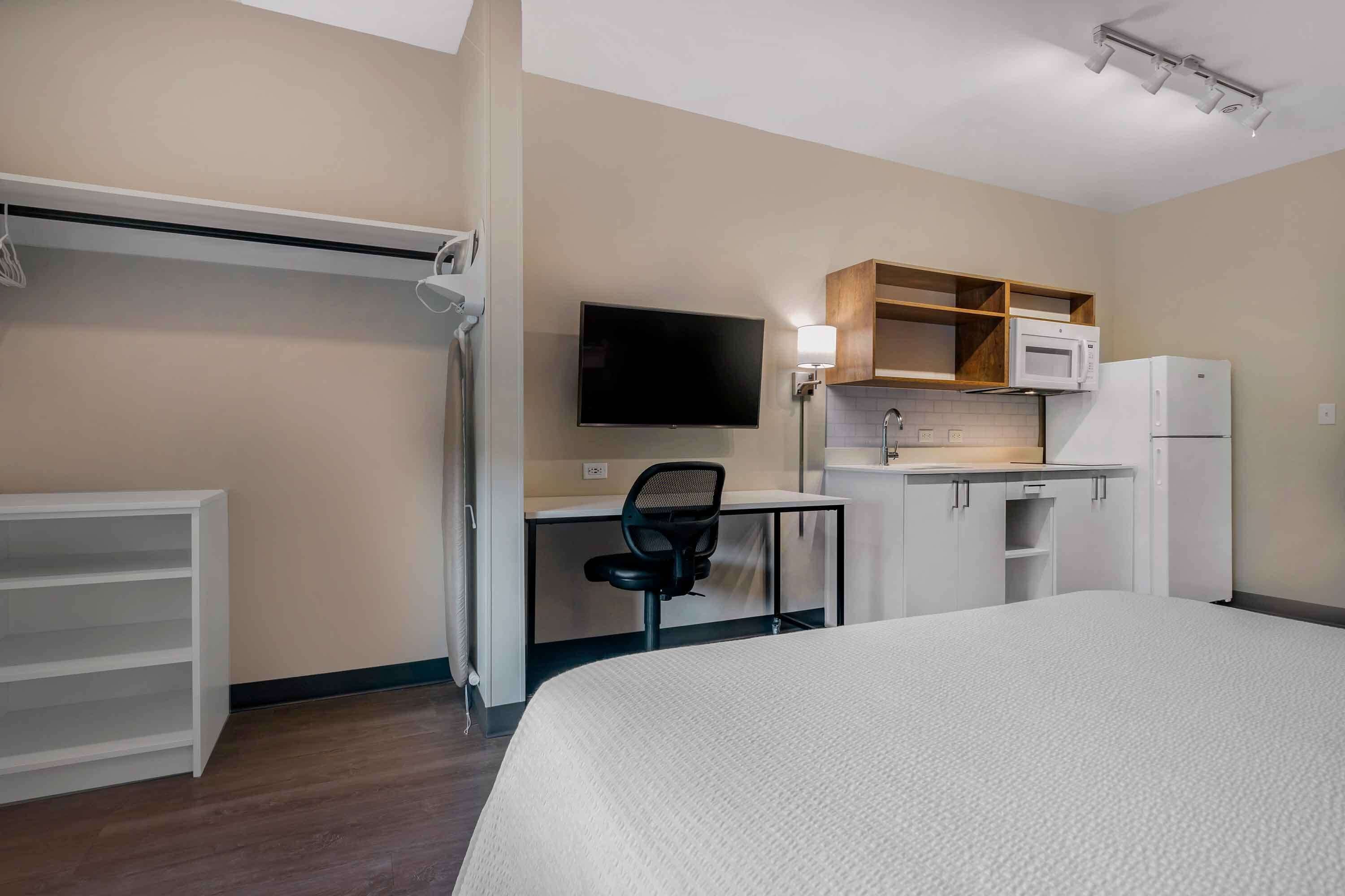Habitación de hotel con cama, escritorio con silla, televisor, microondas y refrigerador.