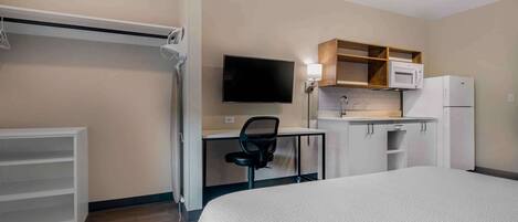 Habitación de hotel con cama, escritorio con silla, televisor, microondas y refrigerador.