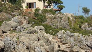 Ein Haus aus Stein mit Ziegeldach, gelegen an einem felsigen Hang mit Blick auf das Meer.