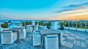 A rooftop terrace with white outdoor furniture, potted plants, and a view of the cityscape. - The Pointe by 360 Blue (Panama City Beach)