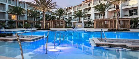 A modern hotel with a central swimming pool, multiple balconies, and palm trees.
