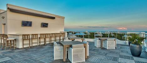 A rooftop terrace with wooden furniture, a bar area, and a view of the ocean.