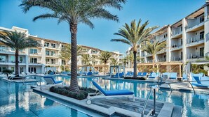 A hotel pool area with multiple lounge chairs and palm trees. - The Pointe by 360 Blue (Panama City Beach)