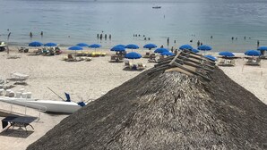 A beach with several blue umbrellas, lounge chairs, and a thatched structure. - Oceanfront condo, beach, pool. 4 eateries on premises. Rent kayaks and jet skis. (Fort Lauderdale)