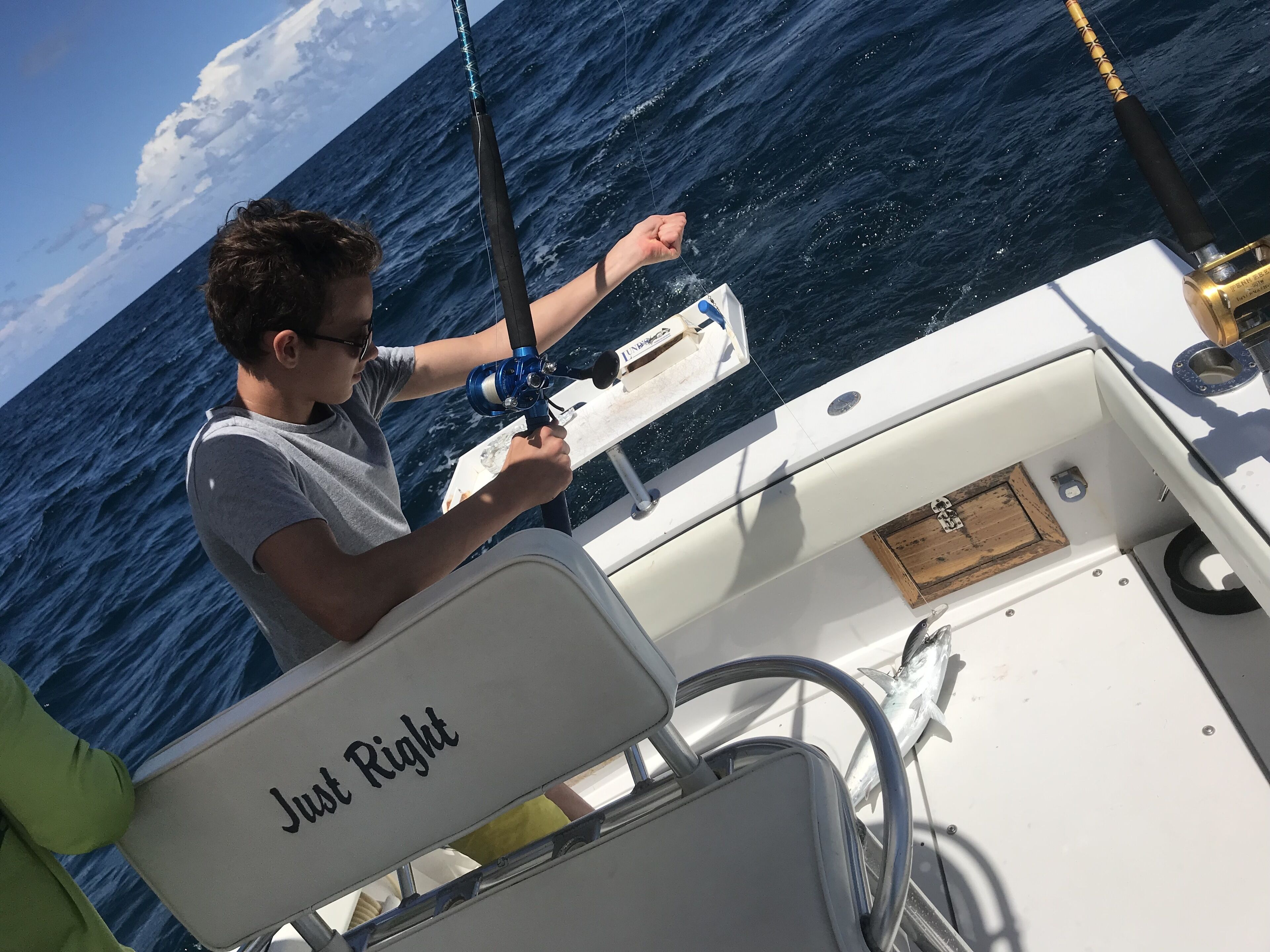 A person fishing on a boat with a white chair labeled "Just Right" and a view of the ocean.