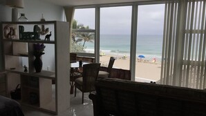 A living room with a view of the beach, a dining area, and a large window with blinds. - Oceanfront condo, beach, pool. 4 eateries on premises. Rent kayaks and jet skis. (Fort Lauderdale)
