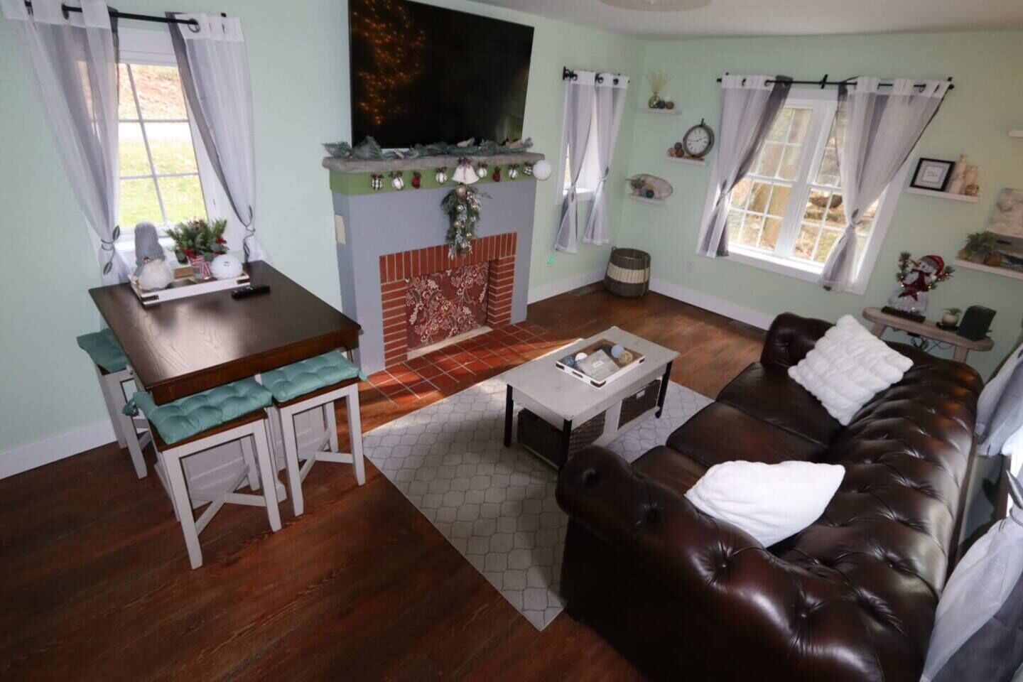 Una sala de estar con chimenea, un sofá de cuero marrón, una mesa de comedor con sillas y un televisor montado en la pared.