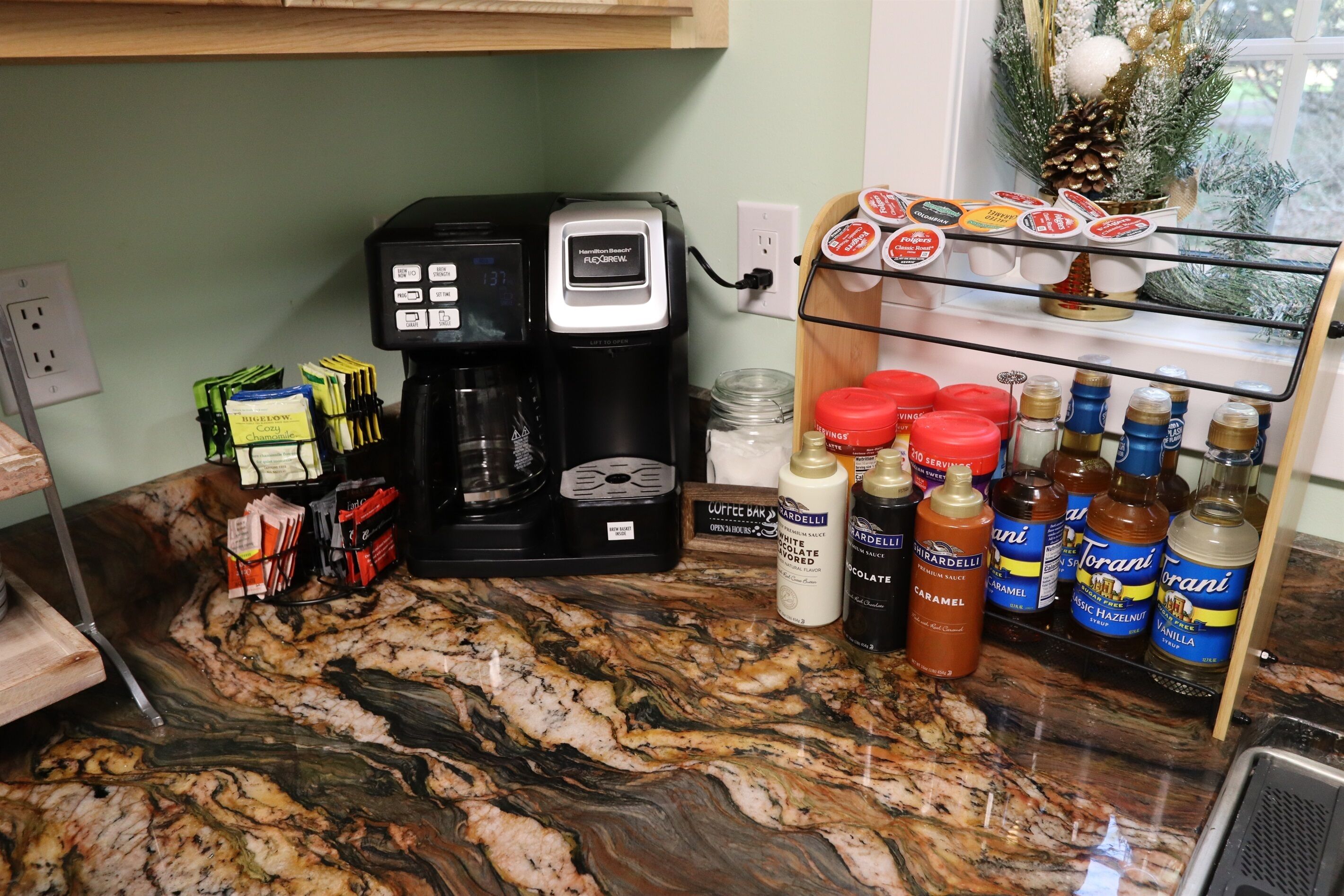 Un piano di lavoro in cucina con una macchina da caffè, cialde per caffè, bustine di zucchero e diversi condimenti.
