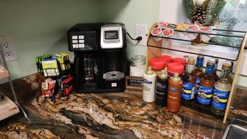 Un piano di lavoro in cucina con una macchina da caffè, cialde per caffè, bustine di zucchero e diversi condimenti.