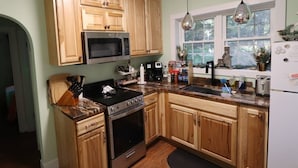 A kitchen with wooden cabinets, a microwave, stove, and a sink. - Romantic Waterfront Cottage for Cherry Springs (Coudersport)